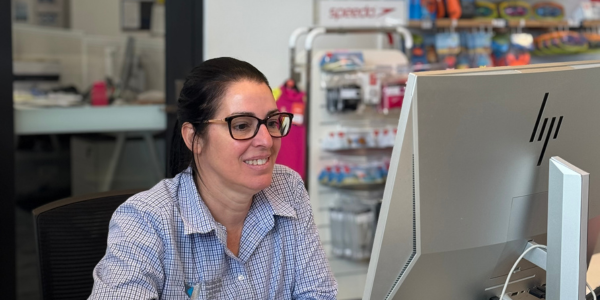 A woman wearing glasses sits at a desk, focused on her computer screen.