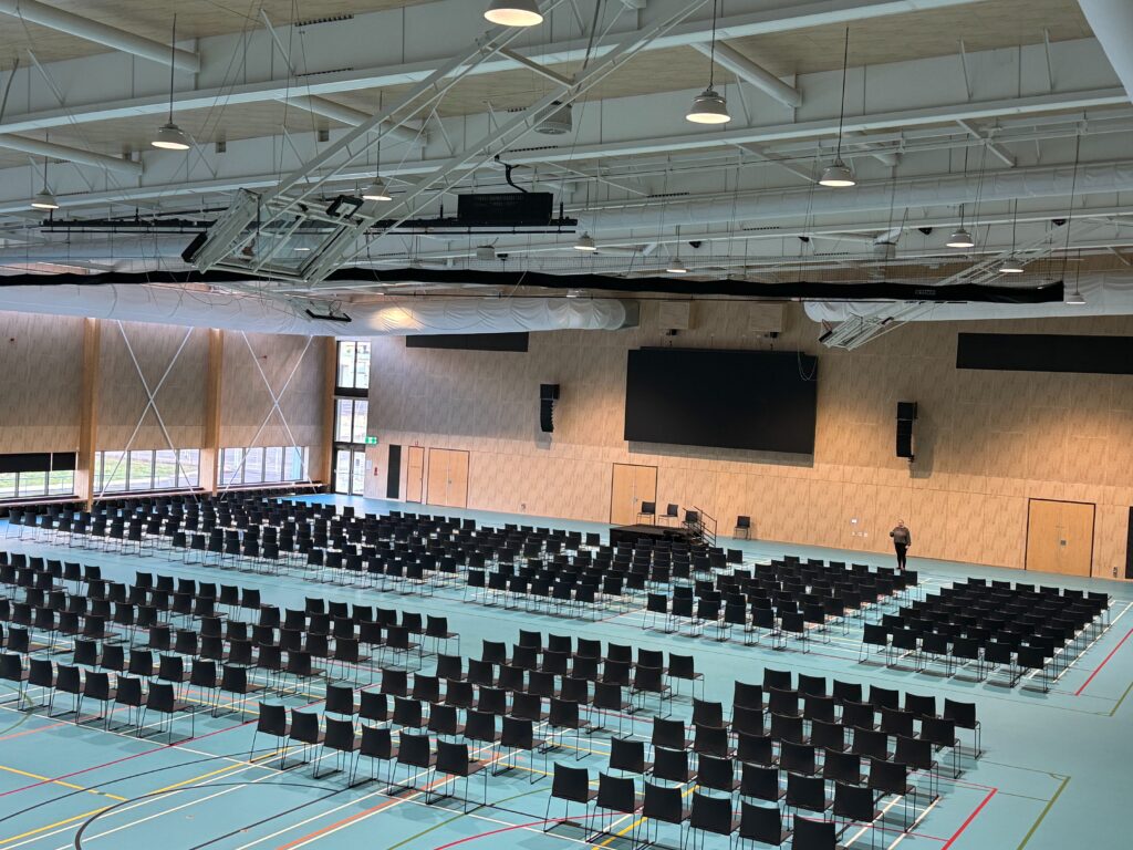 450 chairs in theatre style set in front of a small stage with a large screen behind