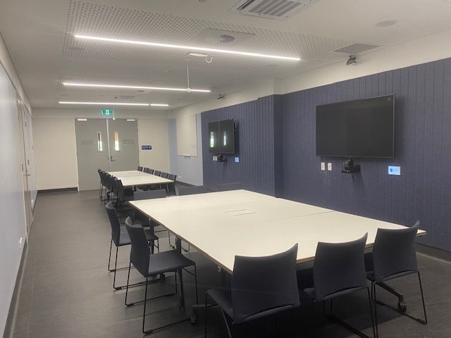Room with two board room tables and two televisions on right hand navy wall