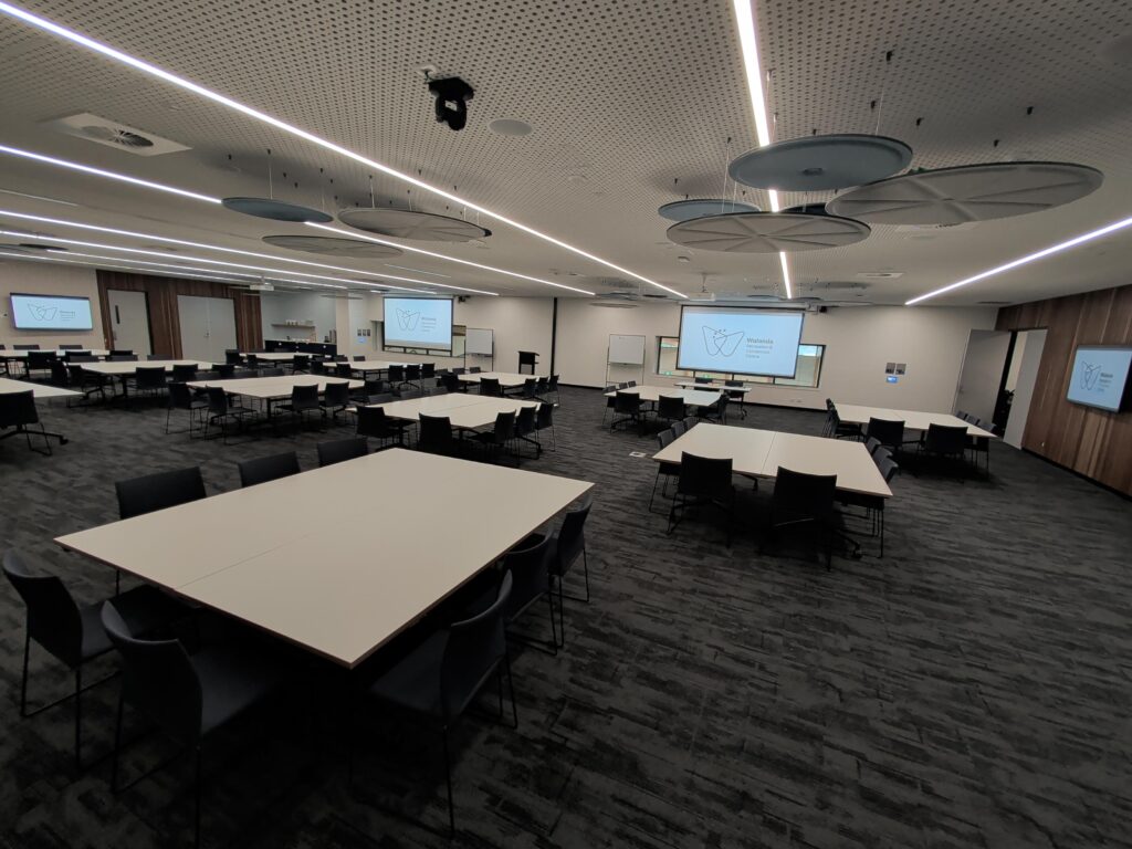 Function Room with two large projector screens showing Wulanda logo, lectern at front and tables set in banquet style
